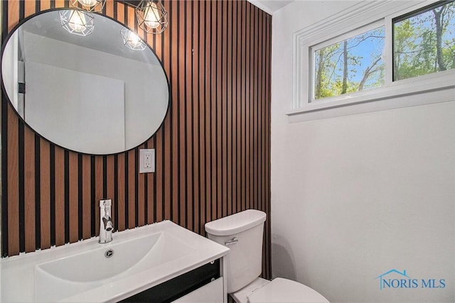 half bathroom featuring toilet, vanity, and wallpapered walls