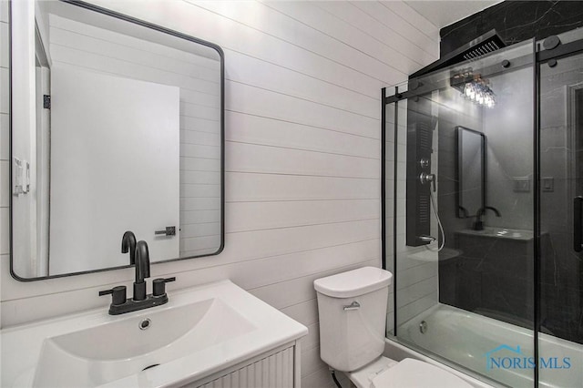 bathroom with wood walls, toilet, bath / shower combo with glass door, and vanity