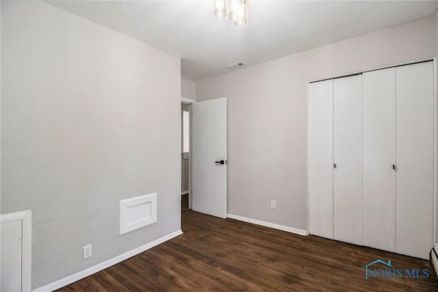 unfurnished bedroom featuring baseboards, dark wood finished floors, a closet, and baseboard heating
