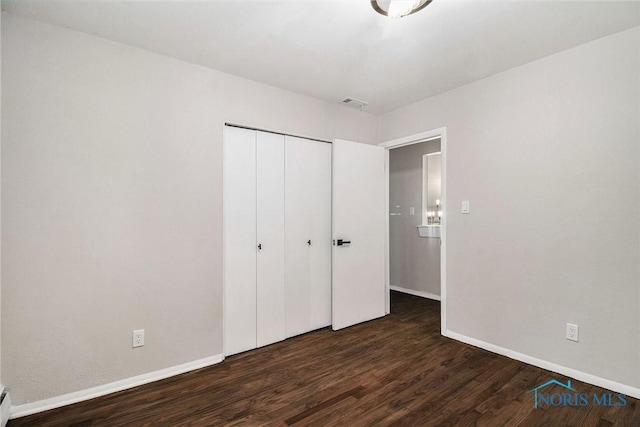 unfurnished bedroom featuring wood finished floors, baseboards, and a closet