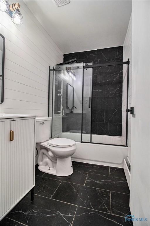 bathroom with marble look tile flooring, toilet, and bath / shower combo with glass door