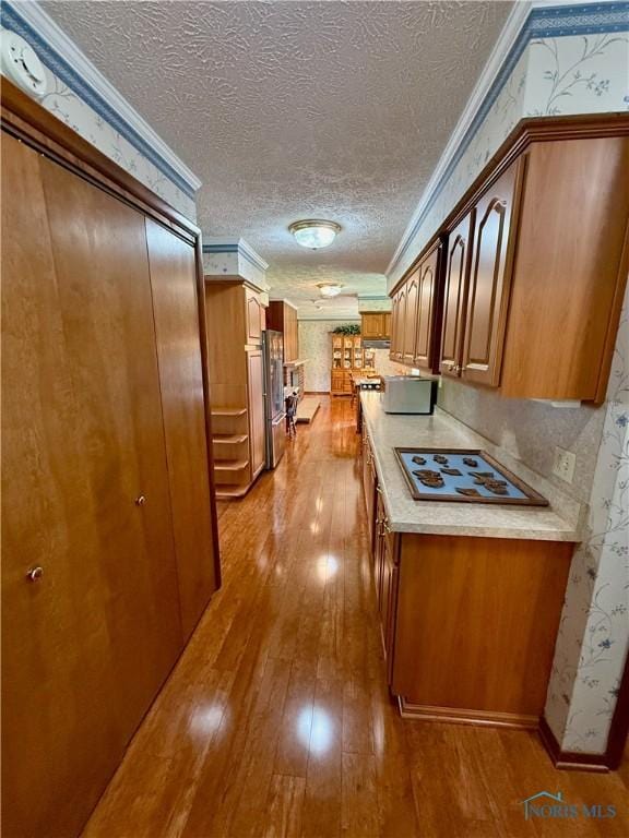 230 Orchard Ln, Upper Sandusky, OH 43351 - kitchen with wood-type flooring, a textured ceiling, crown molding, light countertops, and brown cabinetry