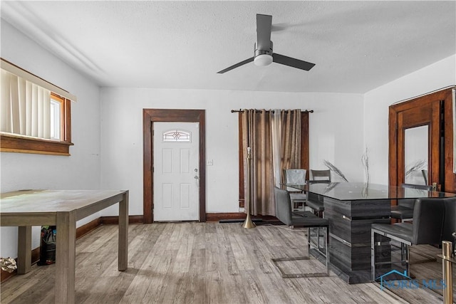 foyer featuring wood finished floors, a ceiling fan, baseboards, and a textured ceiling
