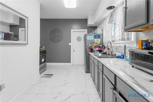 kitchen featuring a sink, light marble finish flooring, gray cabinets, freestanding refrigerator, and baseboards