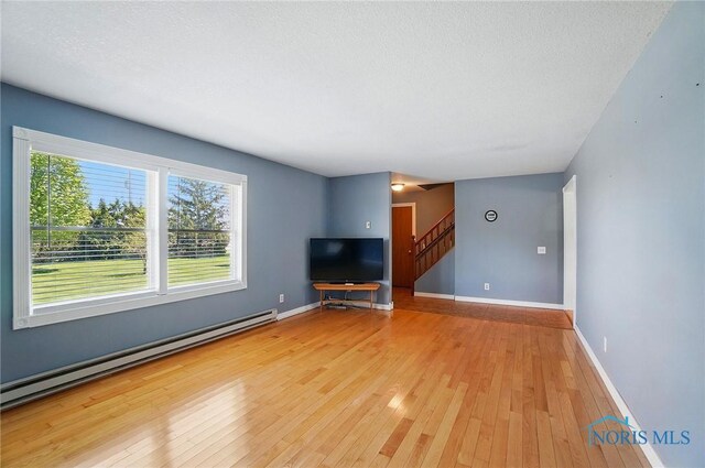 5450 Twp Rd 69, Tiffin, OH 44883 - unfurnished living room with a baseboard radiator, wood-type flooring, stairway, baseboards, and a textured ceiling