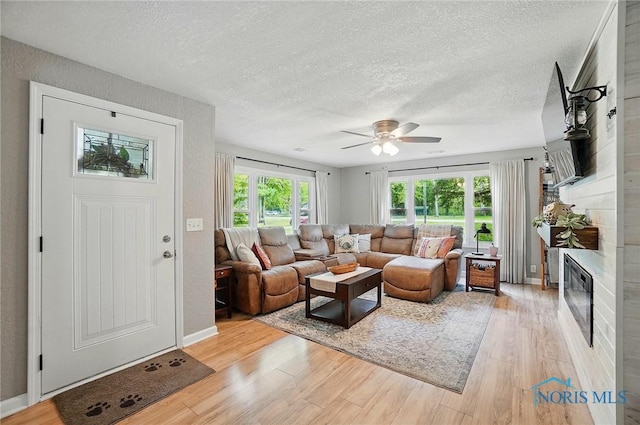 9544 Maumee Western Rd, Monclova, OH 43542 - living area with light wood finished floors, a textured ceiling, ceiling fan, a large fireplace, and baseboards