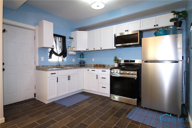 kitchen featuring appliances with stainless steel finishes, a sink, white cabinets, open shelves, and light stone counters