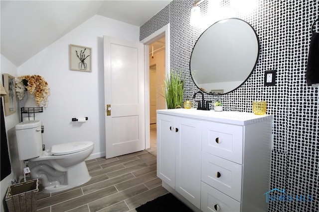 bathroom featuring toilet, wood tiled floors, lofted ceiling, vanity, and baseboards
