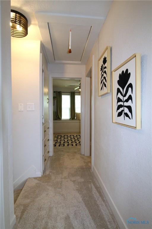 hallway featuring attic access, carpet, and baseboards