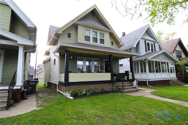 view of front of home with a sunroom, a front yard, covered porch, and roof with shingles
