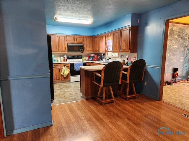 713 Glenwood Rd, Rossford, OH 43460 - kitchen with electric stove, black microwave, light wood-type flooring, brown cabinets, and a textured ceiling
