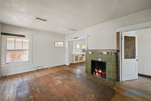 unfurnished living room featuring hardwood / wood-style floors, a tile fireplace, and baseboards