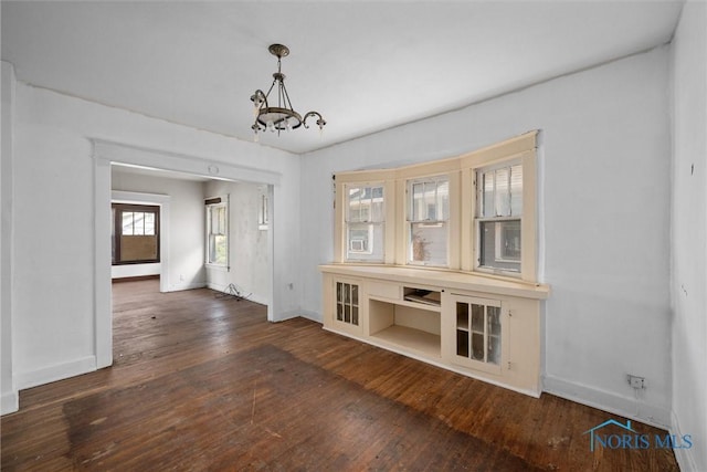 unfurnished dining area featuring baseboards, a chandelier, and wood-type flooring