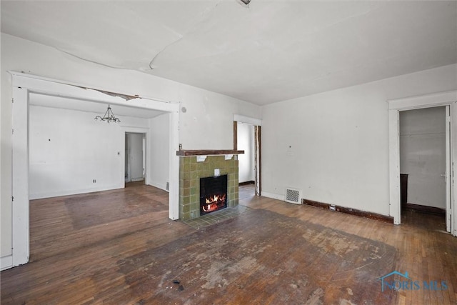unfurnished living room with wood-type flooring, a tile fireplace, a chandelier, and baseboards