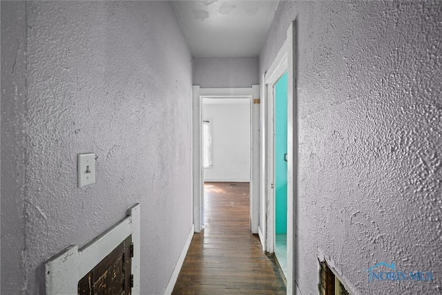 hall featuring wood finished floors, a textured wall, and baseboards