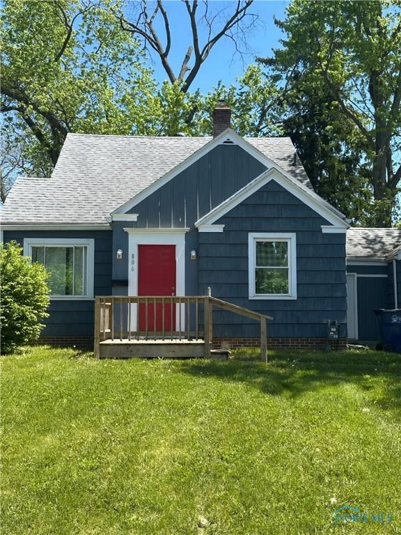 view of front of home featuring a chimney, roof with shingles, a front lawn, and board and batten siding