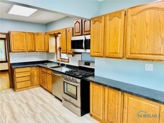 kitchen with stainless steel appliances, a sink, backsplash, dark countertops, and brown cabinets