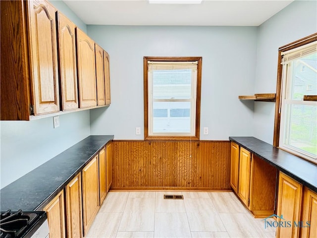 kitchen featuring wainscoting, wood walls, stainless steel range, brown cabinetry, and open shelves