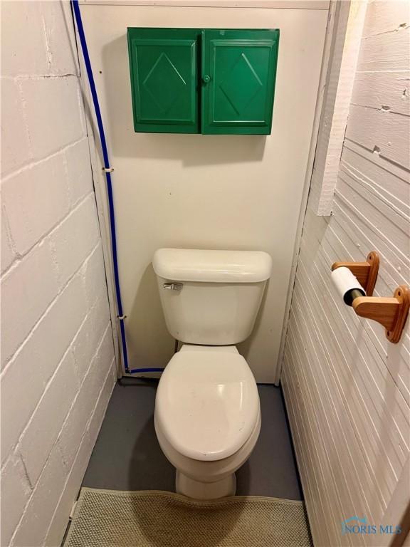bathroom featuring toilet and concrete block wall