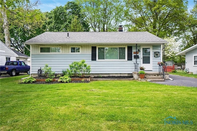 view of front of home featuring a front yard, a chimney, a shingled roof, and board and batten siding