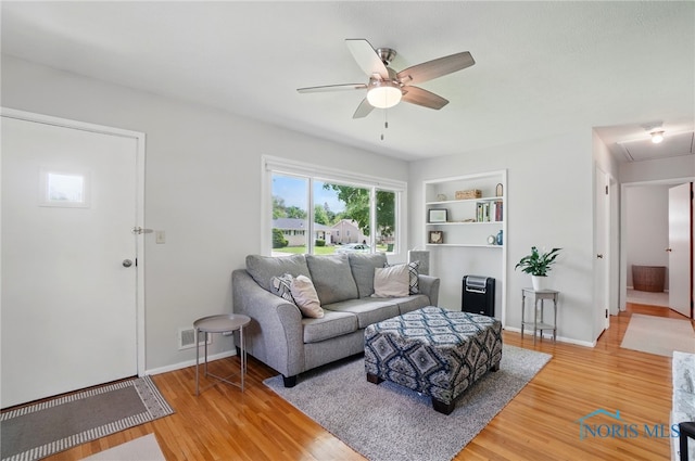 living room with a ceiling fan, light wood finished floors, built in shelves, and baseboards