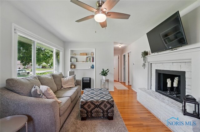 living area with a ceiling fan, light wood-type flooring, built in shelves, and a fireplace