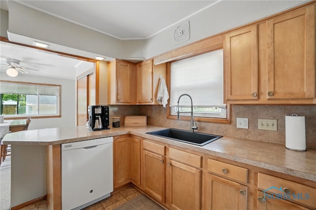 kitchen with white dishwasher, a sink, a peninsula, tasteful backsplash, and light countertops