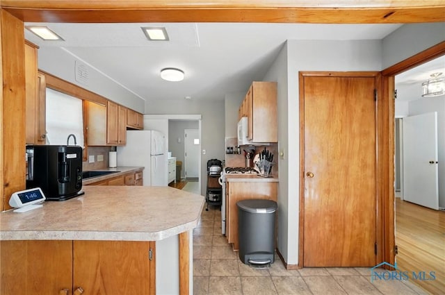 kitchen with white appliances, light countertops, light tile patterned floors, brown cabinets, and a peninsula