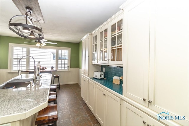 1619 Grant Blvd, Findlay, OH 45840 - kitchen featuring wainscoting, a sink, a kitchen bar, a ceiling fan, and glass insert cabinets