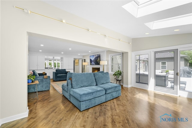 living area with a skylight, wood finished floors, a lit fireplace, recessed lighting, and baseboards