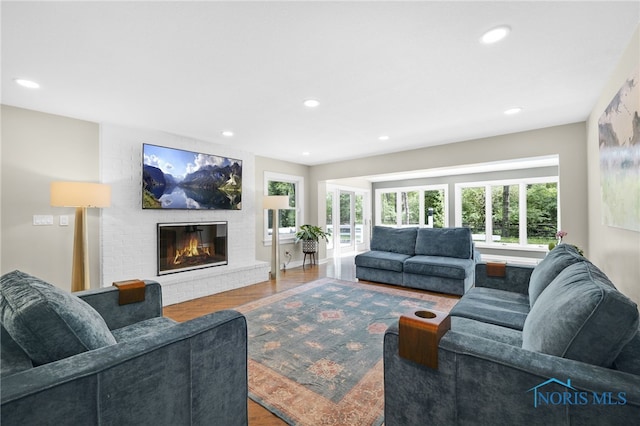 living room with a brick fireplace, wood finished floors, and recessed lighting