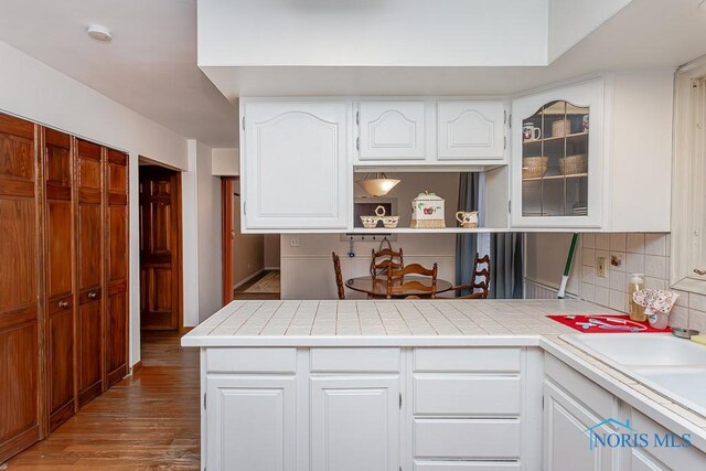 3757 N Mccord Rd, Toledo, OH 43617 - kitchen with decorative backsplash, wood finished floors, a peninsula, white cabinets, and tile countertops