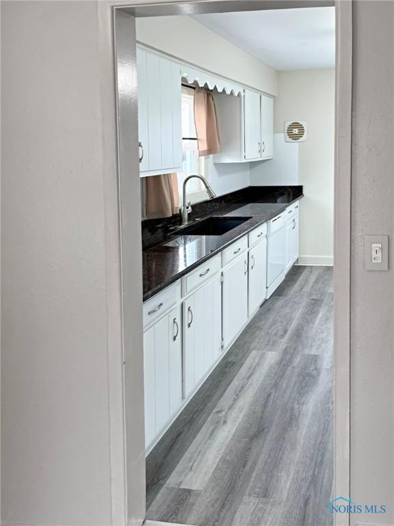 1381 Junior Dr, Maumee, OH 43537 - kitchen featuring dark countertops, a sink, dishwasher, wood finished floors, and white cabinetry