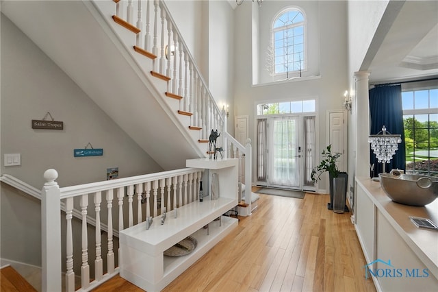 foyer entrance featuring light wood-style flooring, a towering ceiling, and ornate columns