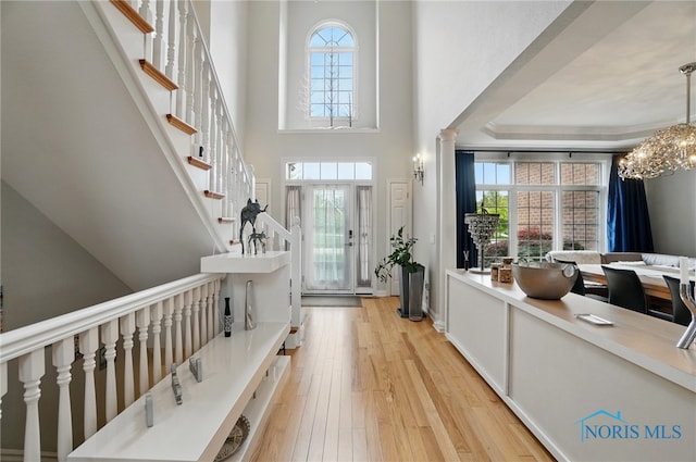 entrance foyer with light wood-style flooring, plenty of natural light, a chandelier, and a towering ceiling