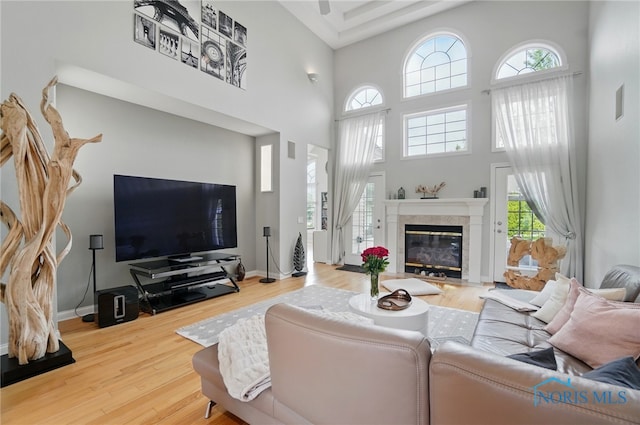living area with plenty of natural light, a high ceiling, wood finished floors, a tile fireplace, and baseboards