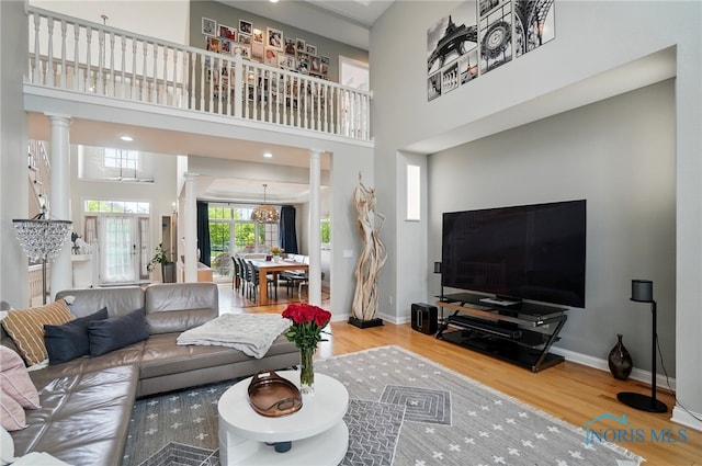 living room with decorative columns, wood finished floors, baseboards, a towering ceiling, and a chandelier