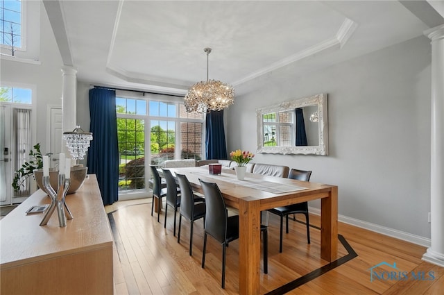 dining area with decorative columns, a raised ceiling, healthy amount of natural light, light wood-style floors, and crown molding