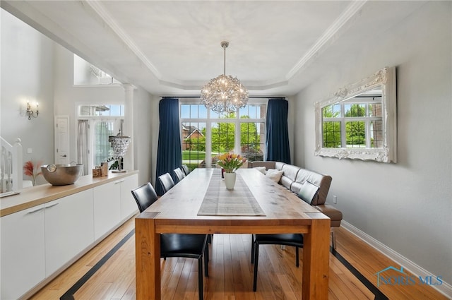 dining space with a raised ceiling, a chandelier, light wood finished floors, healthy amount of natural light, and crown molding