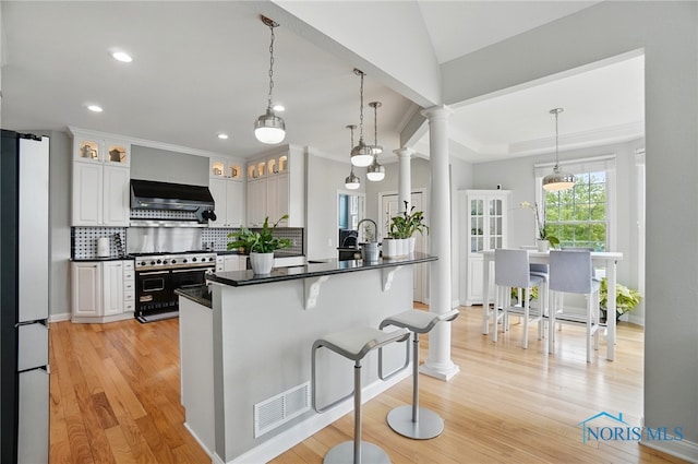 kitchen with exhaust hood, decorative backsplash, light wood-type flooring, double oven range, and a kitchen bar
