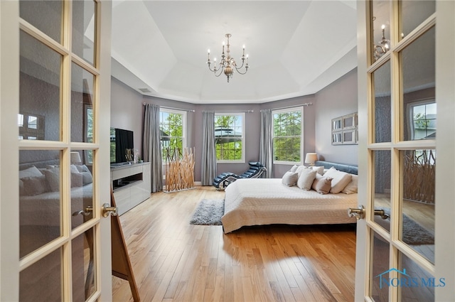 bedroom with a raised ceiling, hardwood / wood-style flooring, a chandelier, and french doors