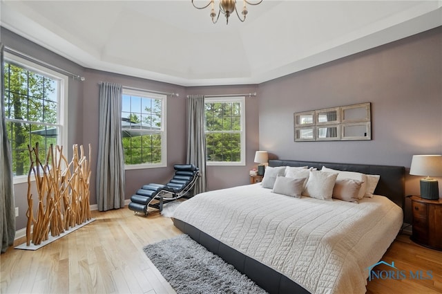 bedroom featuring a raised ceiling, wood finished floors, a chandelier, and baseboards