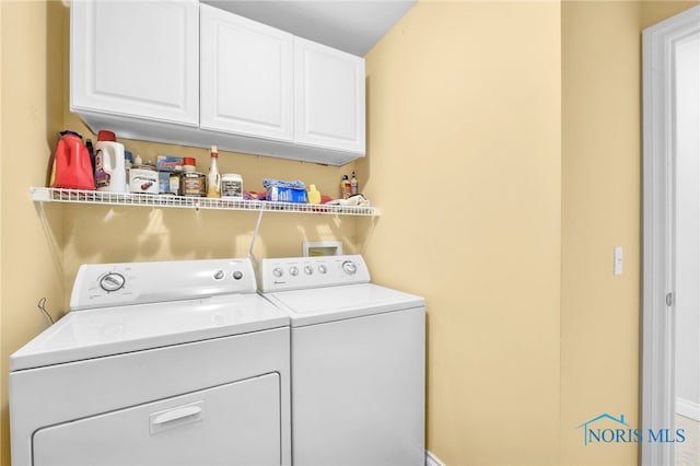 clothes washing area featuring separate washer and dryer, cabinet space, and baseboards