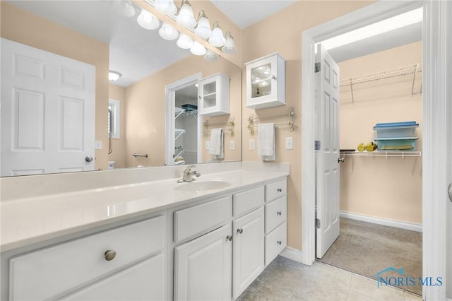 bathroom featuring a walk in closet, vanity, tile patterned floors, and baseboards