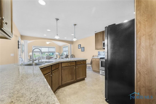 kitchen with ornate columns, a sink, freestanding refrigerator, light countertops, and hanging light fixtures