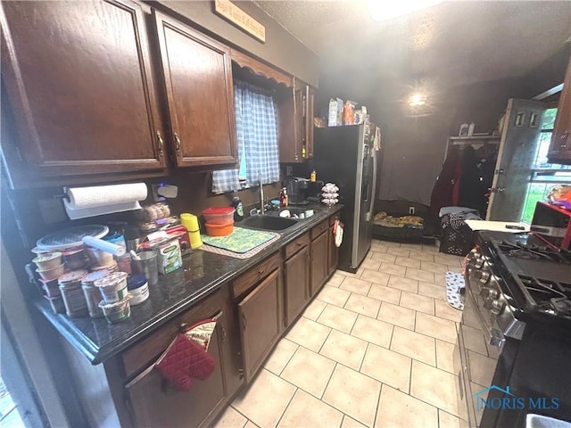 1217 Freedom St, Toledo, OH 43605 - kitchen with gas range oven, dark countertops, light tile patterned floors, freestanding refrigerator, and a sink