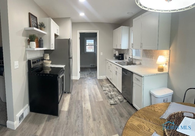 613 W Yeasting St, Gibsonburg, OH 43431 - kitchen featuring a sink, stainless steel appliances, open shelves, light wood-type flooring, and baseboards