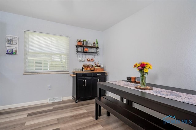 dining area featuring light wood-type flooring, a dry bar, and baseboards