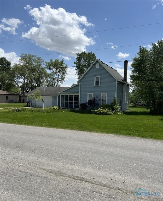 701 E Wayne St, Paulding, OH 45879 - view of side of property featuring a lawn, an attached garage, a sunroom, and a chimney