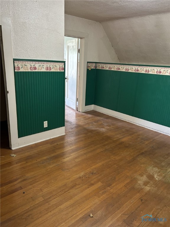 701 E Wayne St, Paulding, OH 45879 - spare room featuring lofted ceiling, wood-type flooring, a textured ceiling, and baseboards